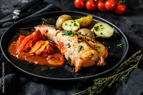 Cooking in tomatoes monkfish fish with baked potatoes. Fresh seafood. Black background. Top view photo
