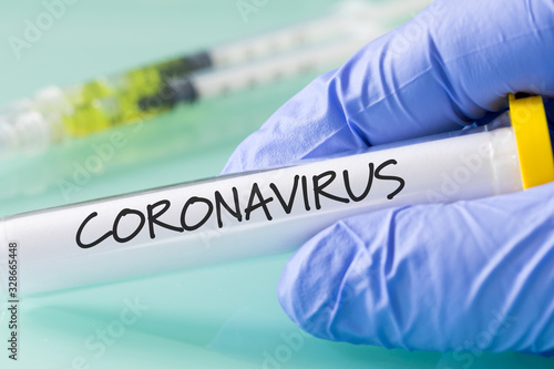 Coronavirus. Laboratory vial with a virus in a hand in a blue glove
