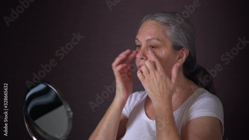 Portrait of senior woman applying an anti-aging cream on her clear face.