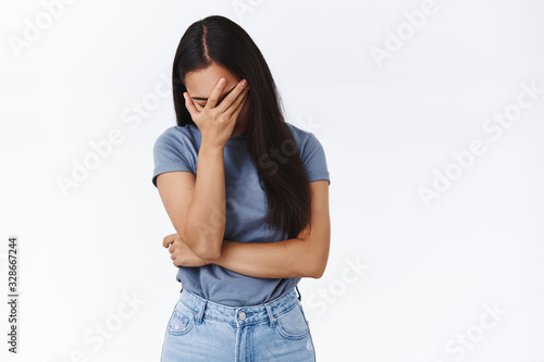 Embarrassed and tired, pissed young asian woman making facepalm, lean on arm and close eyes, sighing fed up, bothered by something humiliating or annoying, standing drained over white background photo