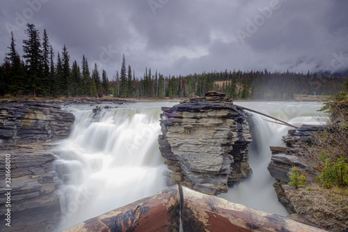 Athabasca Falls in the Rocky Mountains of Canada. Between the cliffs above the water stuck logs. Cloudy day in Jasper National Park