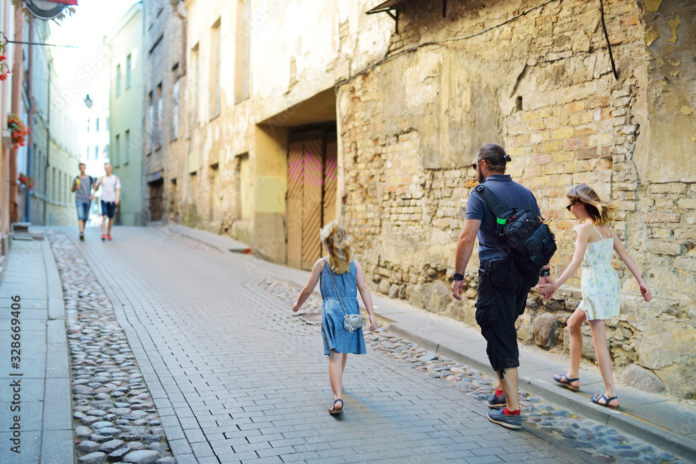 Two cute young girls and their father sightseeing on the streets of Vilnius, Lithuania on sunny summer day.
