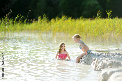 Two young sisters taking healing mud baths on lake Gela near Vilnius, Lithuania. Children having fun with mud. Kids playing with clay.