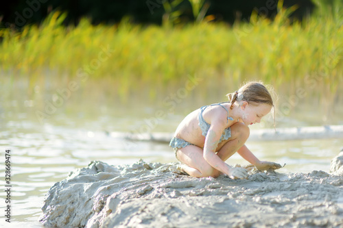 Fototapeta Naklejka Na Ścianę i Meble -  Young girl taking healing mud baths on lake Gela near Vilnius, Lithuania. Child having fun with mud. Kid playing with clay.