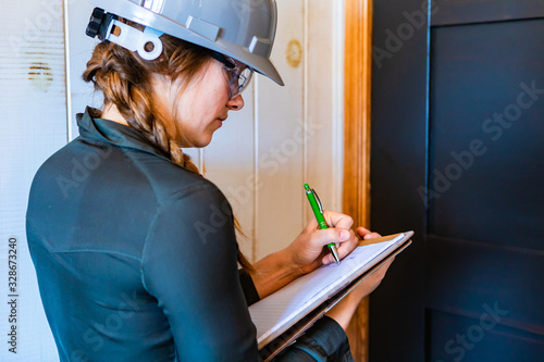 worker woman wears a grey hardhat and protective eyewear at work. female construction inspector taking notes on her clipboard during a home inspection