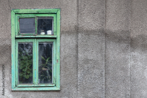 Old gray wall with a green window.