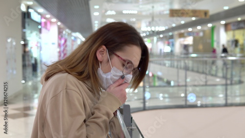 A young woman in a medical mask on the second floor in a shopping center. The woman is coughing. The masked woman protects himself from the epidemic of the Chinese virus "2019-nKoV".