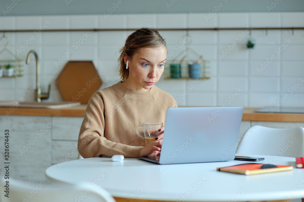 Lovely blonde woman working with her laptop while sitting in the kitchen in her apartment Lovely blonde woman working with her laptop while sitting in the kitchen in her apartment