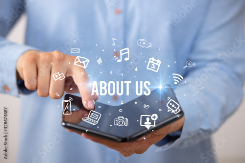 Businessman holding a foldable smartphone with ABOUT US inscription, social media concept