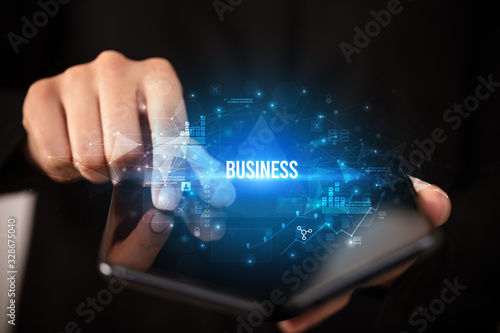 Businessman holding a foldable smartphone with BUSINESS inscription, business concept