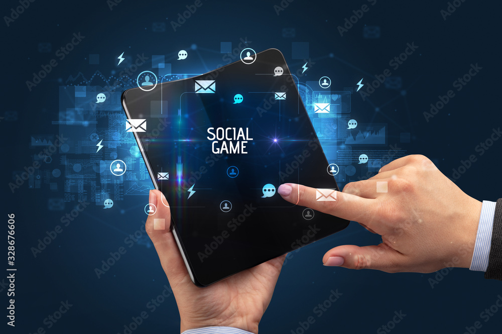 Businessman holding a foldable smartphone with SOCIAL GAME inscription, social networking concept Businessman holding a foldable smartphone with SOCIAL GAME inscription, social networking concept