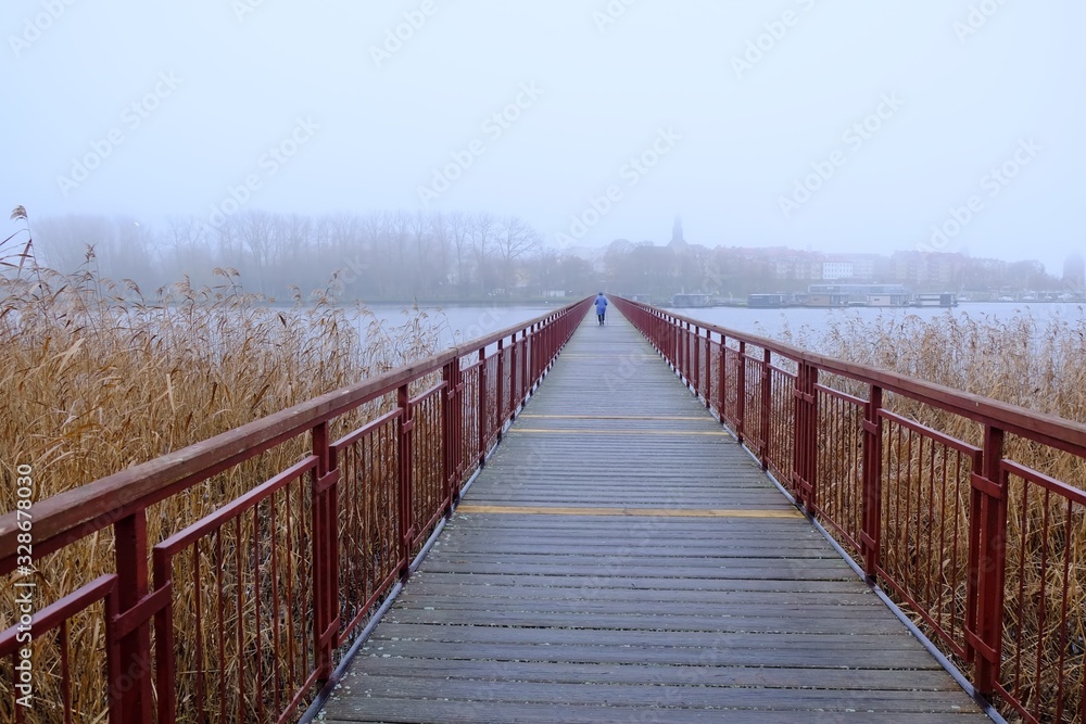 Silhouette of walking person on walkway on the Kamienskie Lake on a misty day, Kamien Pomorski, Poland