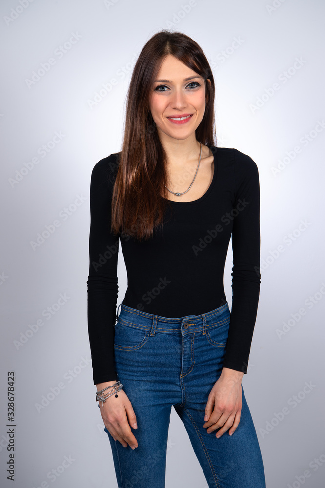 Portrait of pretty woman in blue jeans and black top with hands hanging along her body. Slim beautiful smiling female with long straight brown hair. Portrait of pretty woman in blue jeans and black top with hands hanging along her body. Slim beautiful smiling female with long straight brown hair.