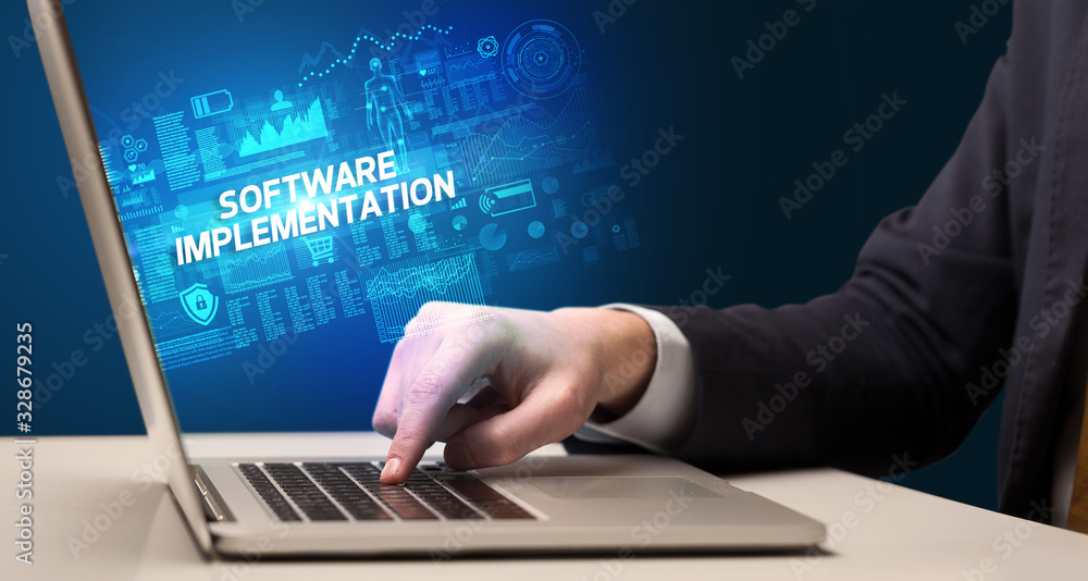 Businessman working on laptop with SOFTWARE IMPLEMENTATION inscription, cyber technology concept Businessman working on laptop with SOFTWARE IMPLEMENTATION inscription, cyber technology concept