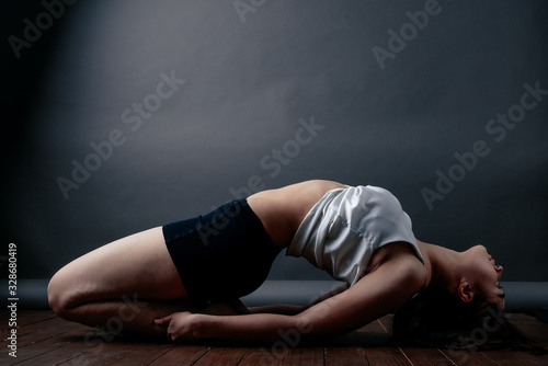 Young attractive girl practicing yoga, stretching in Hero lying exercise, Virasana pose, working out, wearing sportswear for women, black shorts and top, studio gray background