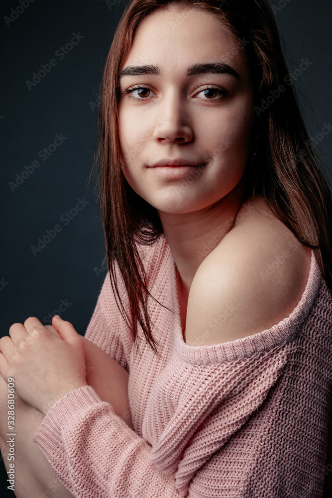 Young beautiful girl poses for a photo. Pink sweater, brunette woman, studio lighting, gray background studio background, portrait, look at the camera. Young beautiful girl poses for a photo. Pink sweater, brunette woman, studio lighting, gray background studio background, portrait, look at the camera.