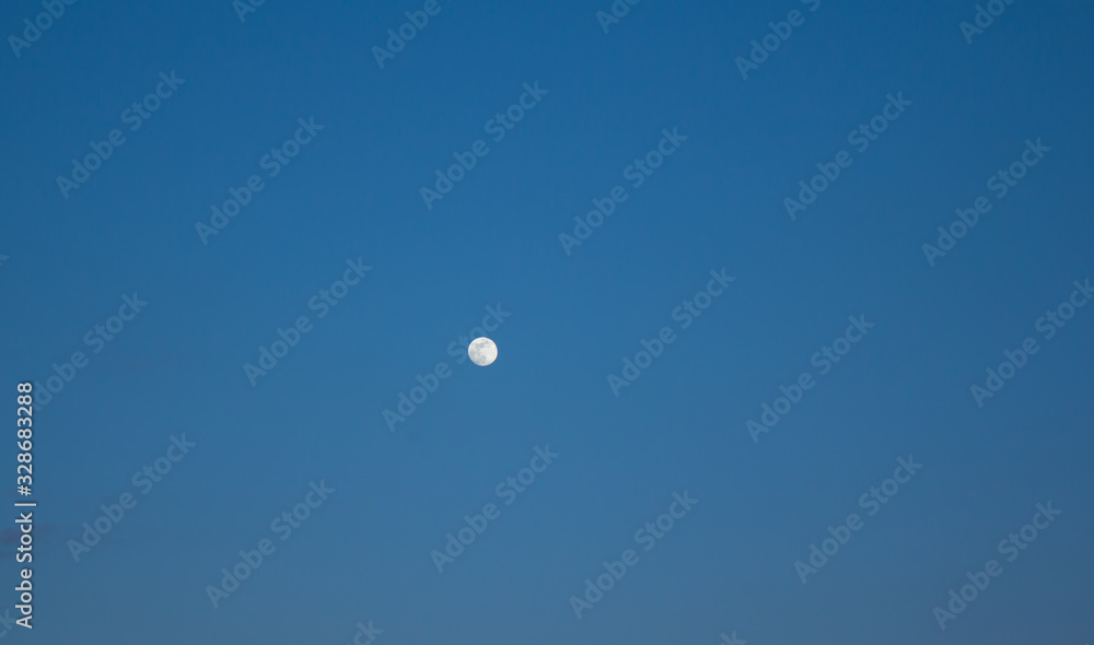 Rising moon in the light blue evening sky Rising moon in the light blue evening sky