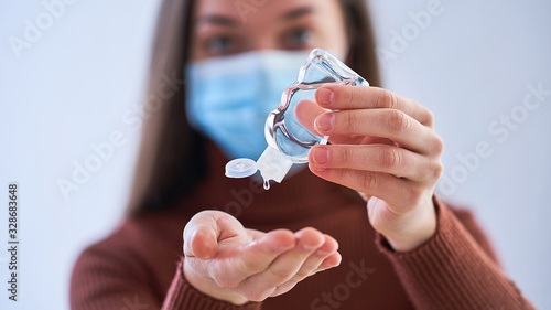 Woman in protective mask applying an antibacterial antiseptic gel for hands disinfection from bacteria. Health protection during flu virus outbreak, and epidemic coronavirus infectious diseases