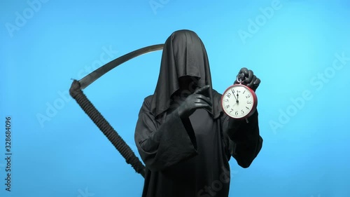 A man in a death suit with a scythe, shows a clock. blue background photo