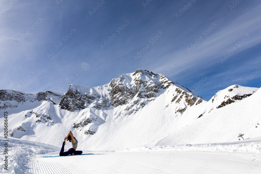 A young woman practice yoga in mountains. With a great view of snow and winter landscape.