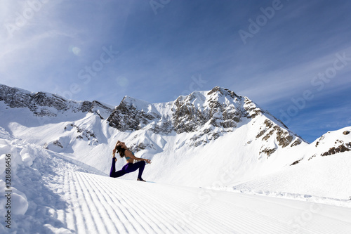 A young woman practice yoga in mountains. With a great view of snow and winter landscape.