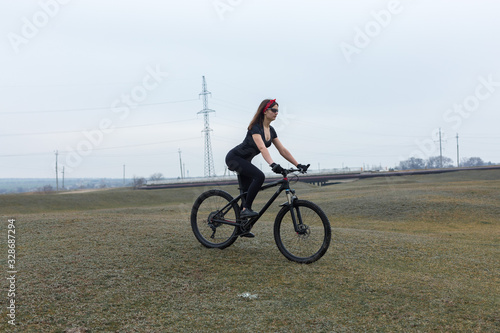 Girl on a mountain bike on offroad, beautiful portrait of a cyclist at sunset, Fitness girl rides a modern carbon fiber mountain bike in sportswear. Close-up portrait of a girl in a helmet and glasses