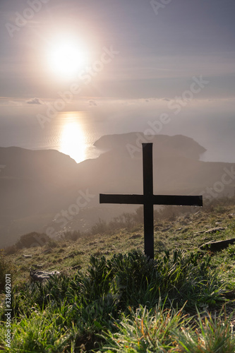 Paisaje al amanecer con cruz en primer plano y el sol al fondo con el mar en el Cap de Creus (Cataluña, España)