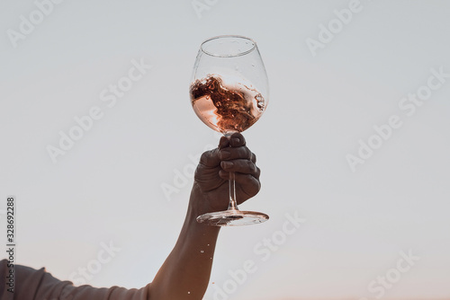 Glass of wine with splashes in woman's hand against the sunset sky.