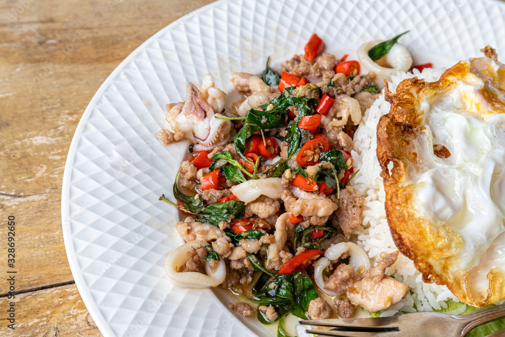 Stir fried squid basil and minced pork with steamed rice and fried egg on a white plate. Stir fried squid basil and minced pork with steamed rice and fried egg on a white plate.