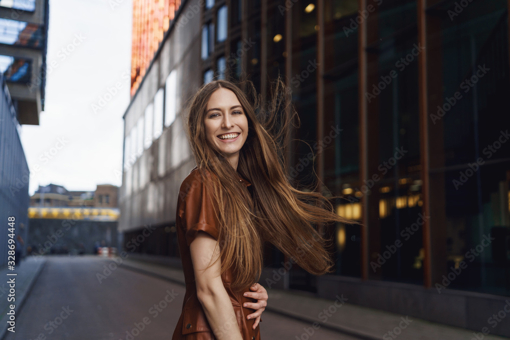 Waist-up outdoor portrait of charismatic gorgeous woman having fun, feeling happy, laughing as turn back to smile camera, walking along empty city street near business buildings