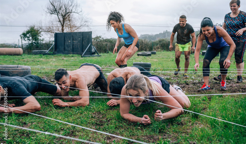 Group of participants in an obstacle course crawling under electrified cables photo