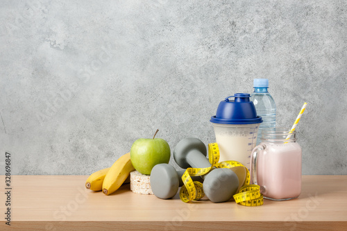 Fototapeta Naklejka Na Ścianę i Meble -  Protein cocktail, dumbbells, measuring tape, water bottle and fresh fruits on wooden table