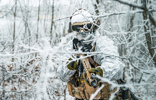 Airsoft man in white camouflage uniform and machinegun with optical sight. Soldier in the winter forest between branches. Horizontal photo.