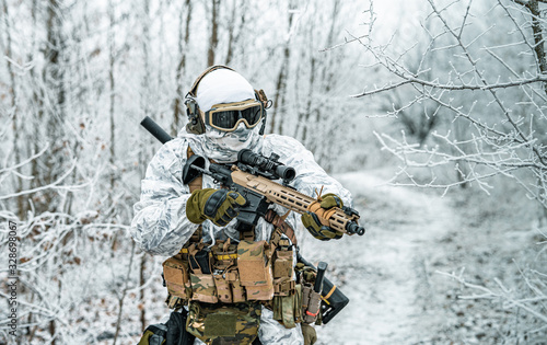 Airsoft man in white camouflage uniform and machinegun with optical sight. Soldier in the winter forest between branches. Horizontal photo.