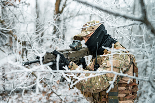 Airsoft man in camouflage uniform and machinegun with optical sight. Soldier in the winter forest. Side view.