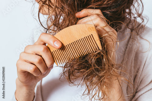Young woman combing tangled ends of her curly hair photo