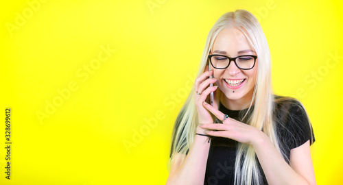 Young blonde girl calls and talks on the phone, on a yellow studio background. Positive leisure. Communication