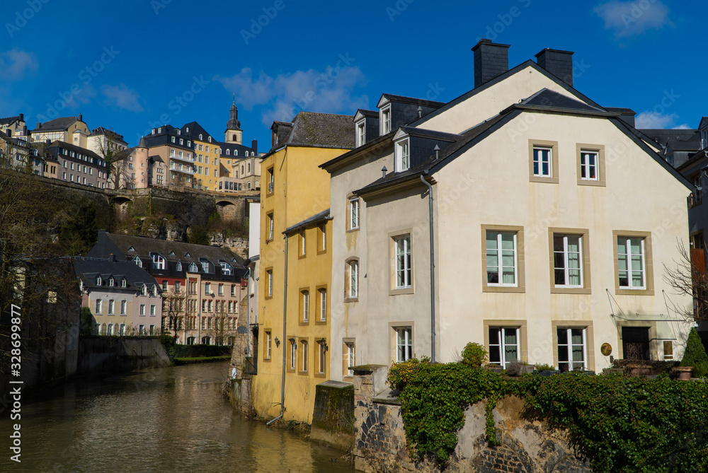 Blue sky view of beautiful medieval pastel colorful houses on the river in Luxembourg City Grund (lower city) neighborhood with the upper city in the background