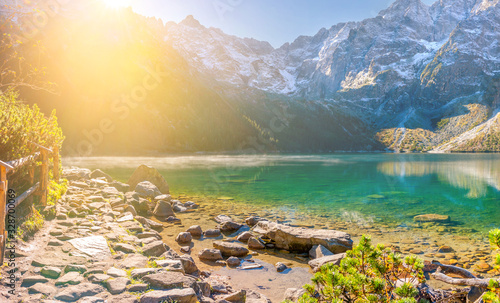 Fototapeta Naklejka Na Ścianę i Meble -  Beautiful view of the mountain lake at sunrise in the Tatra Mountains. Morning fog over the lake in the Polish Tatra National Park. Mountain range in the rays of the rising sun.