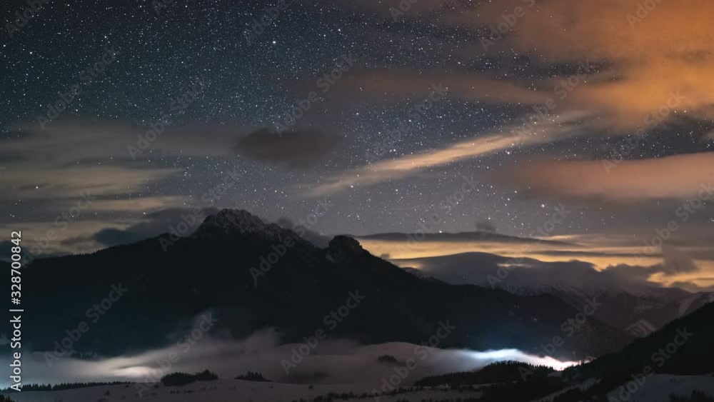 Panoramic view of Starry night sky with stars and colorful clouds in winter mountains with mist in valley time lapse Panoramic view of Starry night sky with stars and colorful clouds in winter mountains with mist in valley time lapse