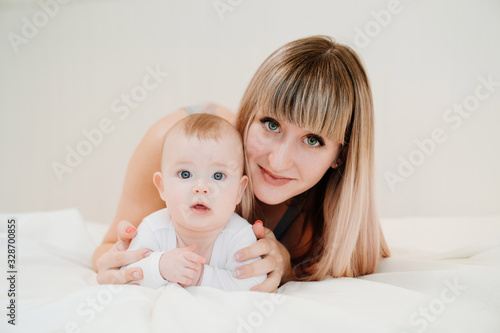 mom and baby lie on white bed and look at camera.