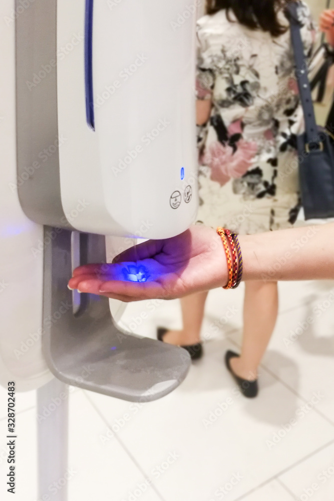 Person cleaning hand with anti-bacterial hand disinfectant from sanitizer dispenser in public mall Person cleaning hand with anti-bacterial hand disinfectant from sanitizer dispenser in public mall