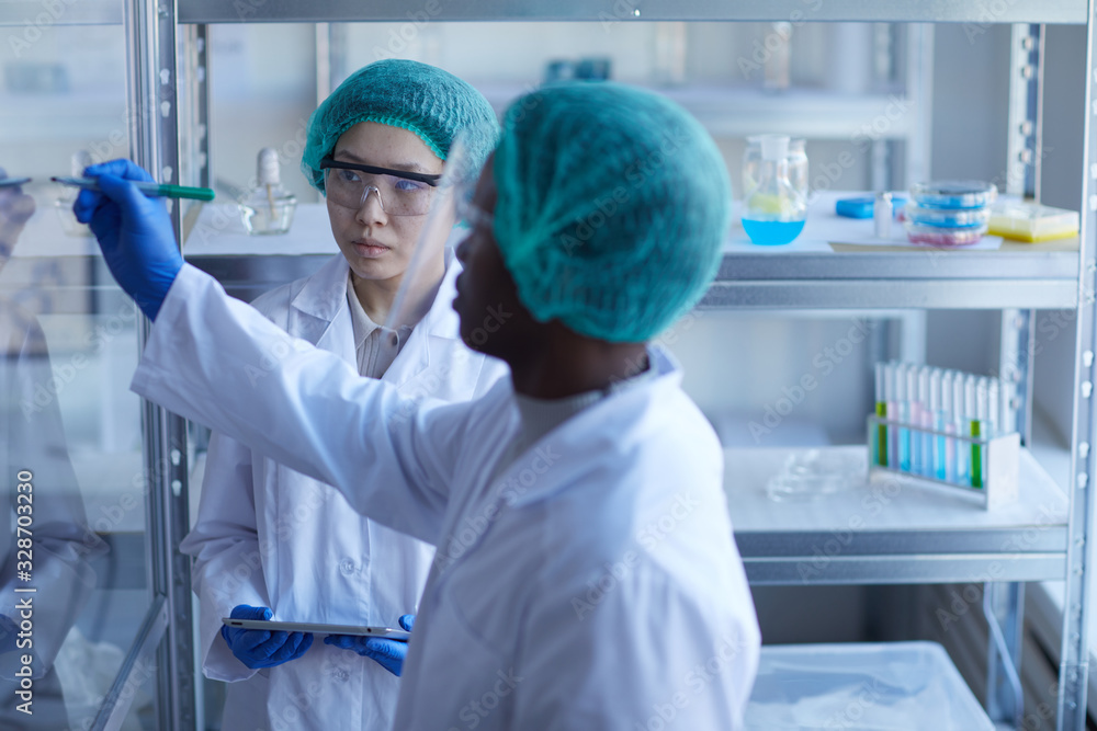 Horizontal portrait of Black male laboratory worker writing formula on glass wall, his female Asian colleague looking at it Horizontal portrait of Black male laboratory worker writing formula on glass wall, his female Asian colleague looking at it