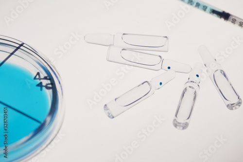 Horizontal high angle close up shot of petri dish with specimen, glass ampoules with medication and syringe on white surface