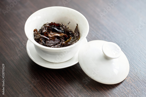 Chinese porcelain gaiwan for tea ceremony or gong fu cha or kung fu tea for brewing oolong, on wooden table or chaban with wet tea leaves close up.