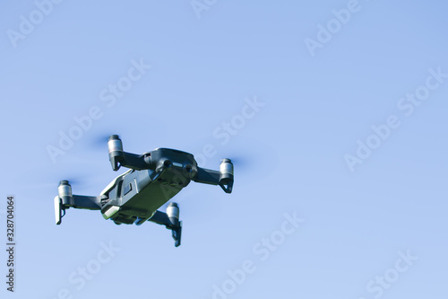Fototapeta Naklejka Na Ścianę i Meble -  Four-propeller drone flying in nature against the blue sky. The maneuver.