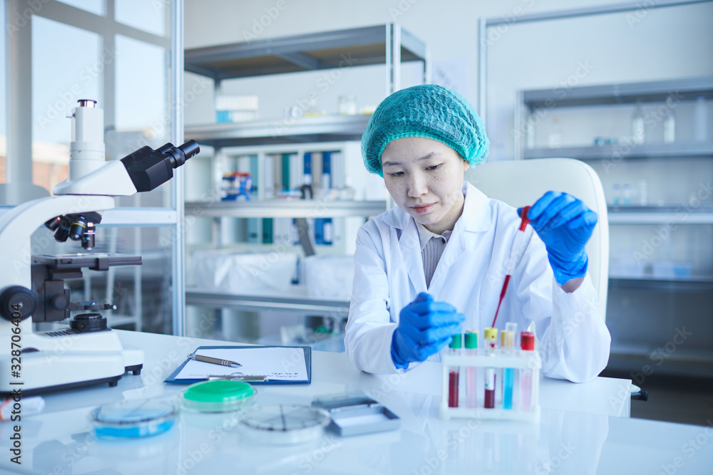 Horizontal portrait of concentrated young woman wearing lab coat, protective gloves and hat doing medical tests, copy space Horizontal portrait of concentrated young woman wearing lab coat, protective gloves and hat doing medical tests, copy space