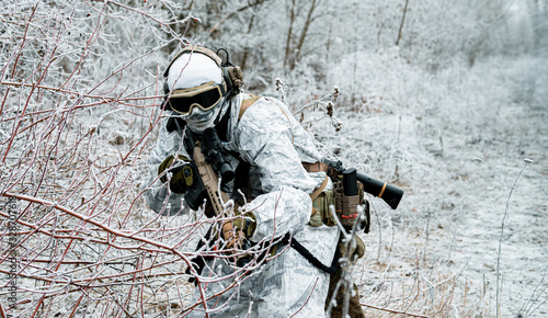Military man in white camouflage uniform with machinegun. Soldier sneaking in the winter forest with machinegun. Front view.