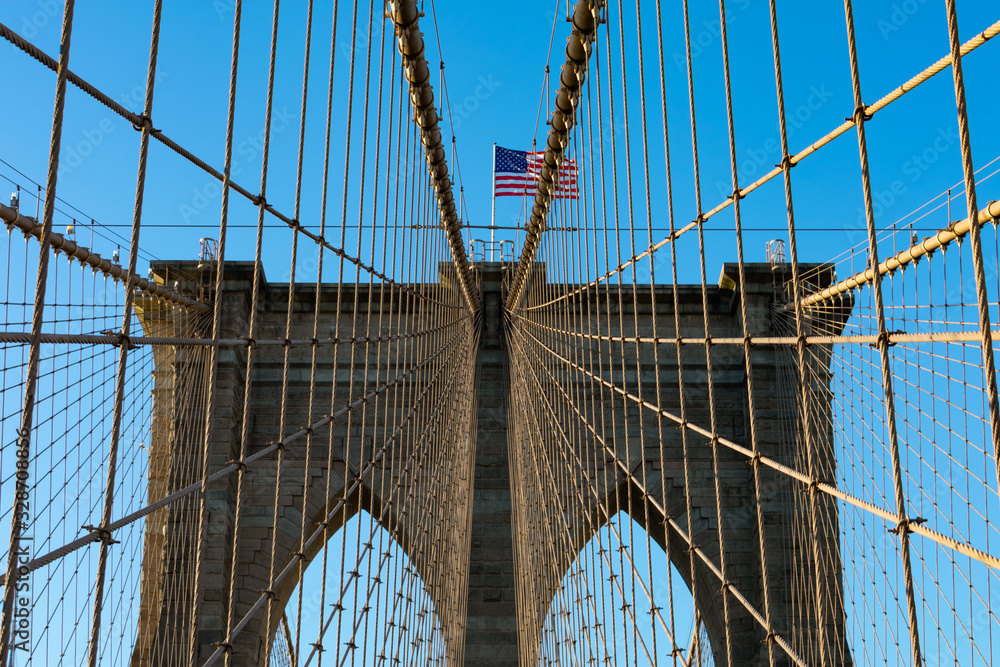 Obraz premium Arches on the Brooklyn Bridge with an American Flag in New York City and a Blue Sky