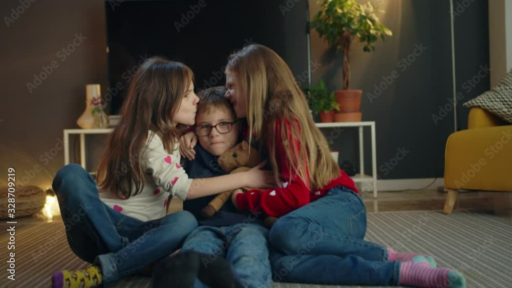 Cheerful Caucasian lovely young kids triplets having fun together in modern living room, attractive little brother and sisters kissing and hugging sitting on floor carpet in casual jeans indoors Cheerful Caucasian lovely young kids triplets having fun together in modern living room, attractive little brother and sisters kissing and hugging sitting on floor carpet in casual jeans indoors